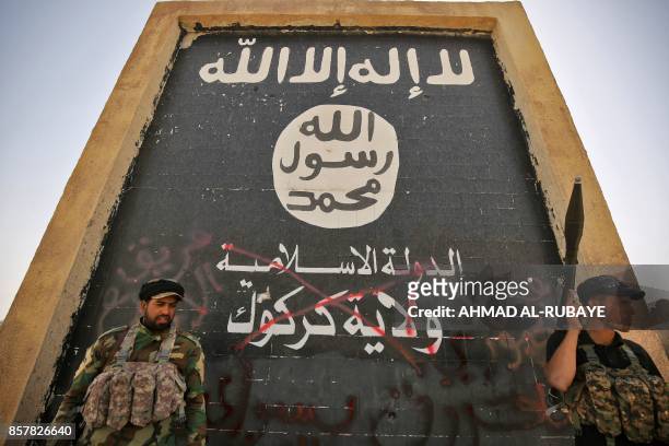 Fighters from the Hashed al-Shaabi , backing the Iraqi forces, stand in front of a mural depicting the emblem of the Islamic State group as troops...