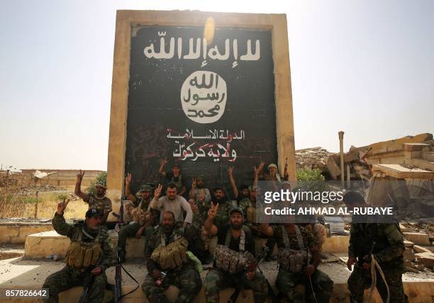 Fighters from the Hashed al-Shaabi , backing the Iraqi forces, pose in front of a mural depicting the emblem of the Islamic State group as troops...