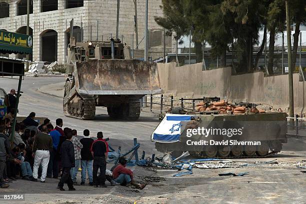 Palestinians watch an Israeli army armored personnel carrier, decorated with an Israeli flag, and an armored bulldozer advance through the al-Amari...