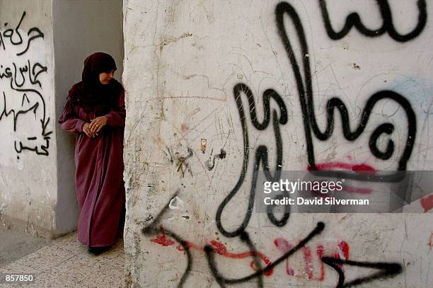 Palestinian woman stands between graffiti-covered walls outside her home March 12, 2002 in the al-Amari refugee camp as the sounds of battle...