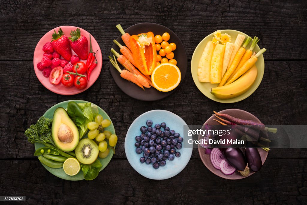 Plates with various coloured fruit & vegetables on a black surface.