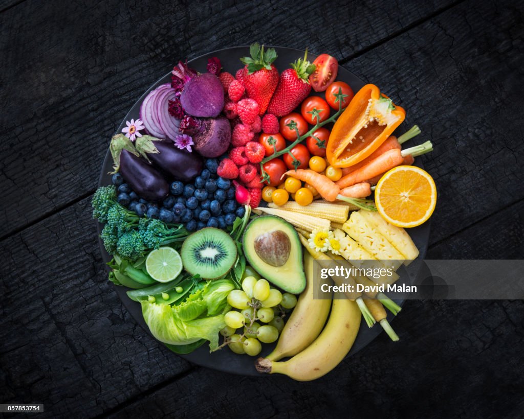 Multicoloured fruit and vegetables in a black bowl on a burnt surface.