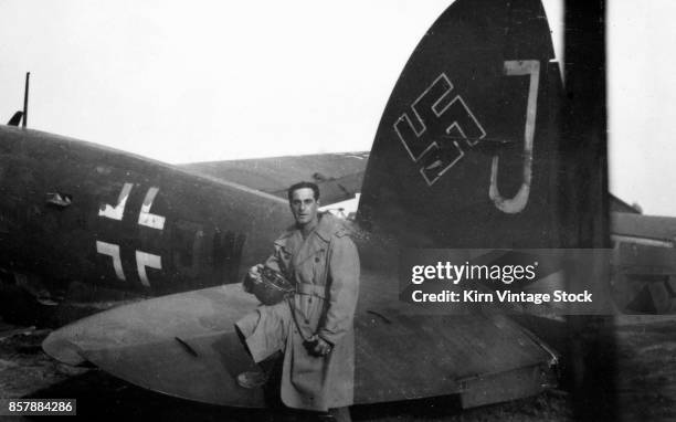 Army soldier poses by the tail fin of a captured German plane during the liberation of France. The plane has both swastika and luftwaffe markings.