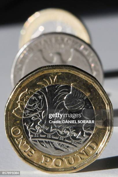 British one pound sterling coin, a one euro coin and a US quarter dollar coin are arranged and photographed in central London on October 5, 2017. -...