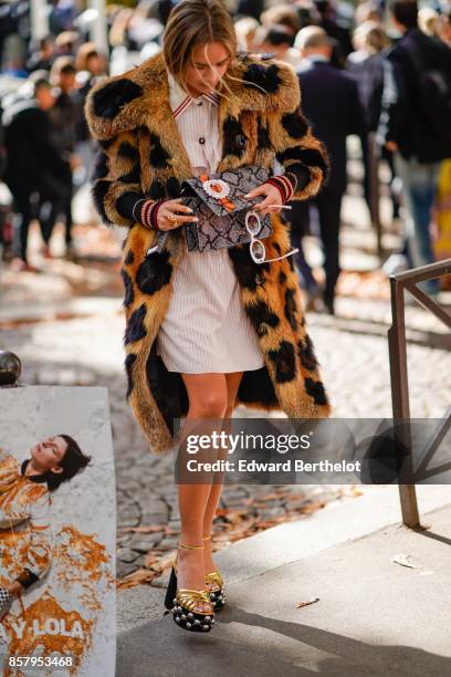 Guest wears a leopard print fur coat, a white dress, a snake print bag, outside Miu Miu, during Paris Fashion Week Womenswear Spring/Summer 2018, on...