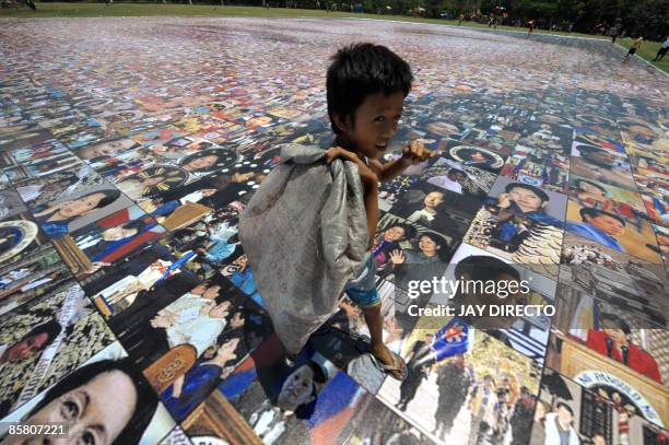 Child scavenger looks at a photo mosaic of Philippine President Gloria Arroyo set up at Luneta park in Manila on April 5, 2009. Supporters of...