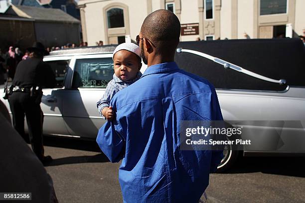 Father holding a child stands in front of a hearse in the parking lot of the Islamic Organization of the Southern Tier following funeral prayers for...