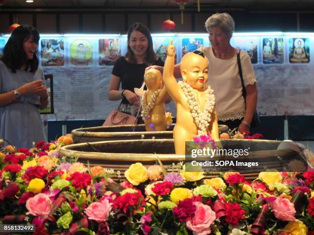 Buddhist family devotees pours water to statue of Buddha on the Wesak day. Wesak is the most important day for Buddhist devotees as they commemorates...