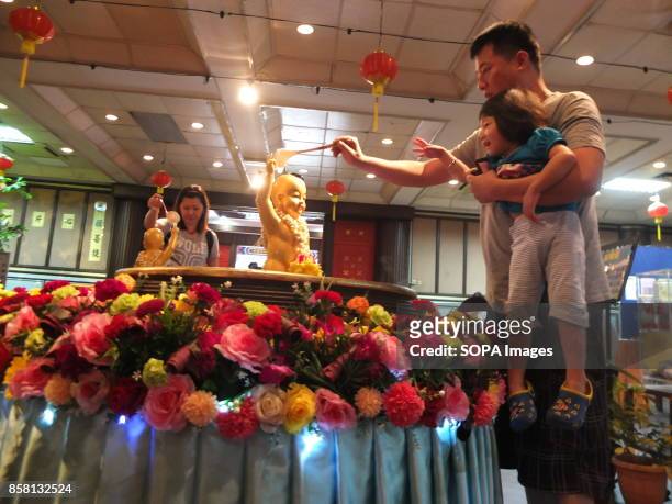 Buddhist family devotees pours water to statue of Buddha on the Wesak day. Wesak is the most important day for Buddhist devotees as they commemorates...