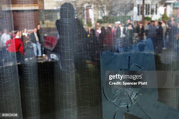 Reflected in a window with a bullet hole, over one hundred people gather with flowers in front of the American Civic Association to pay their...