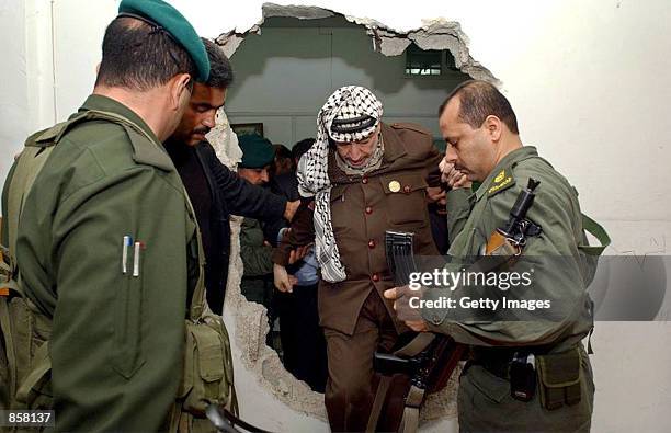 With the help of his bodyguards, Palestinian leader Yasser Arafat climbs March 16, 2002 through a hole in the wall made by Israeli troops during...