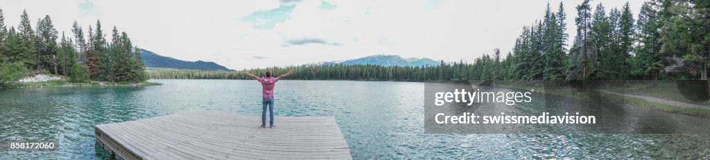 Panoramic of young man arms outstretched on lake pier