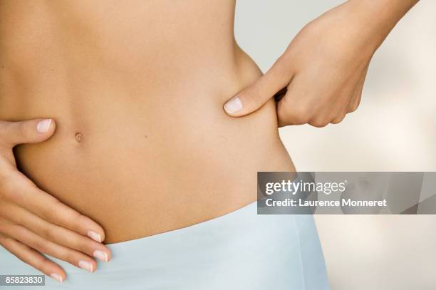 closeup on a young woman pinching her waist - magro foto e immagini stock