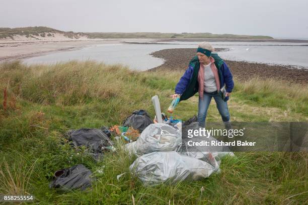 Woman throws a drinks bottle on to a pile of assorted plastic materials awaiting removal from the coastal landscape, having been collected by...