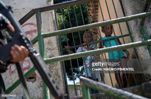 Local children stand behind a fence as Brazilian Armed Forces soldiers keep watch at the Morro dos Macacos favela during a security operation in the...