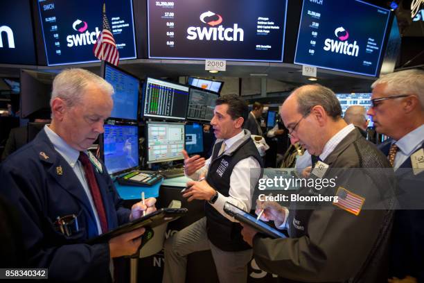 Traders work beneath a monitor displaying Switch Inc. Signage on the floor of the New York Stock Exchange in New York, U.S., on Friday, Oct. 6, 2017....