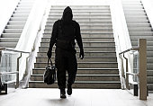Hooded Lone wolf Man wearing black carrying bag in urban underground public transport setting