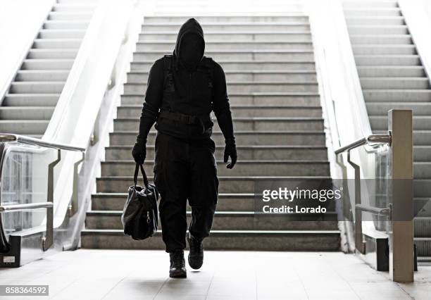 hooded lone wolf man wearing black carrying bag in urban underground public transport setting - terrorism stock pictures, royalty-free photos & images