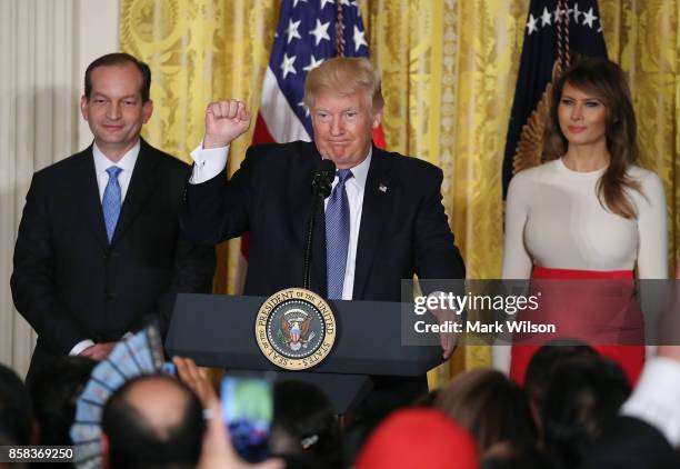 President Donald Trump is flanked by Labor Secretary Alex Acosta and first lady Melania Trump as he speaks to guests gathered in the East Room of the...