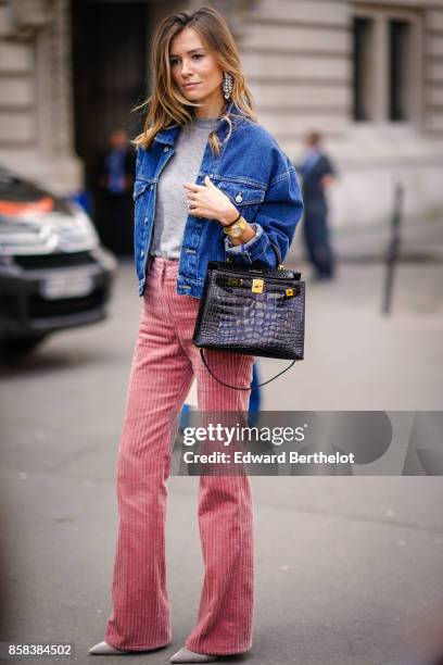 Guest wears a blue denim jacket, a crocodile black leather bag, a gray top, pink flare pants, outside Moncler, during Paris Fashion Week Womenswear...
