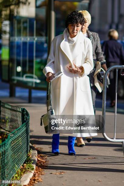 Guest wears a white coat, blue shoes, a chanel bag, outside Chanel, during Paris Fashion Week Womenswear Spring/Summer 2018, on October 3, 2017 in...