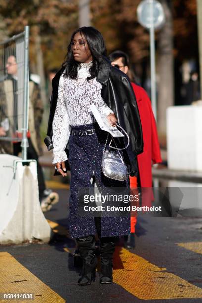 Guest wears a black leather jacket, a white lace top, flare pants, black boots, silver bag, outside Chanel, during Paris Fashion Week Womenswear...