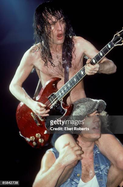 Photo of Angus YOUNG and AC/DC and Brian JOHNSON and AC DC; Angus Young playing guitar sitting on Brian Johnson's shoulders