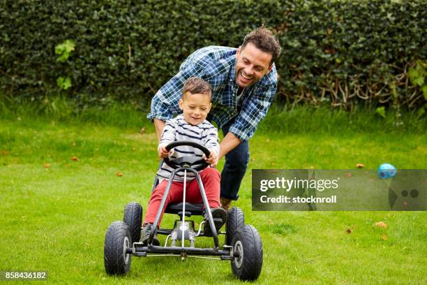 ragazzo carino in sella a pedalata con padre in giardino - macchina a pedali foto e immagini stock