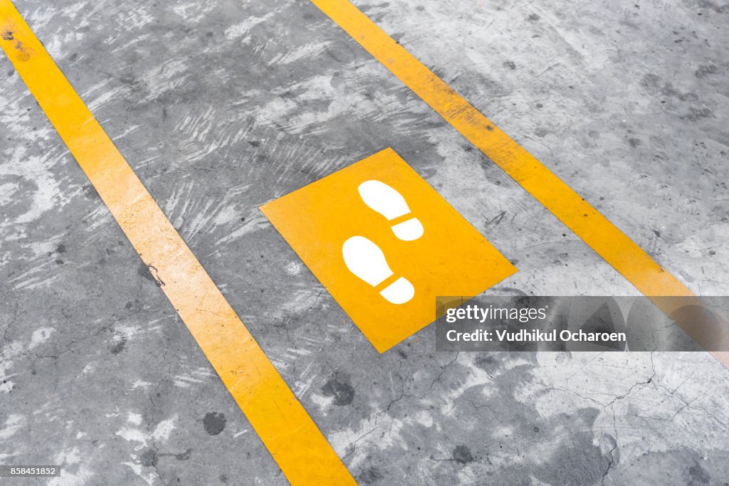 Walkway lane in parking building. Painted yellow footsteps between parallel yellow lines on abstract cement floor.