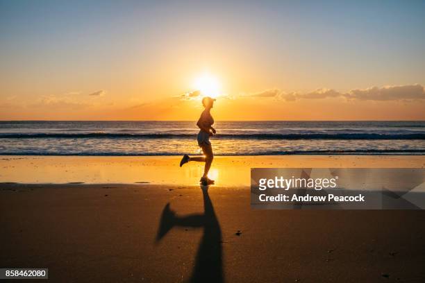 a woman is running on the beach at sunrise. - noosa beach fotografías e imágenes de stock