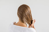 Woman in the white towel with comb brushing her wet blonde hair after shower on the gray background. Cares about a healthy and clean hair. Beauty salon concept.