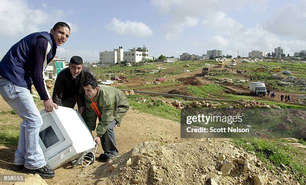 Palestinian men carry a washing machine past a makeshift crossing March 27, 2002 north of the West Bank town of Ramallah. Many of the roads...
