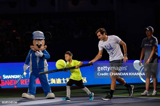 Roger Federer of Switzerland assists a child during a friendly tennis match with Disney characters Mickey mouse and Goofy at the Shanghai Rolex...
