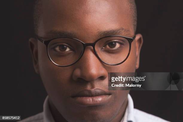 portrait of young man with dark skin standing in front of black background, close-up. - black glasses stock-fotos und bilder