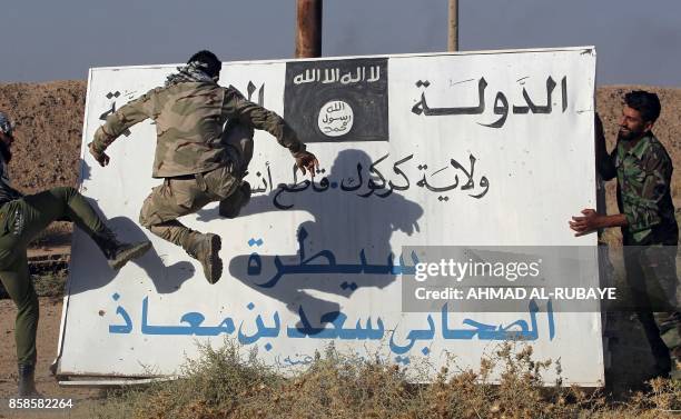 Fighters from the Hashed al-Shaabi , backing the Iraqi forces, kick a billboard bearing the logo of the Islamic State group in Hawija on October 6 a...