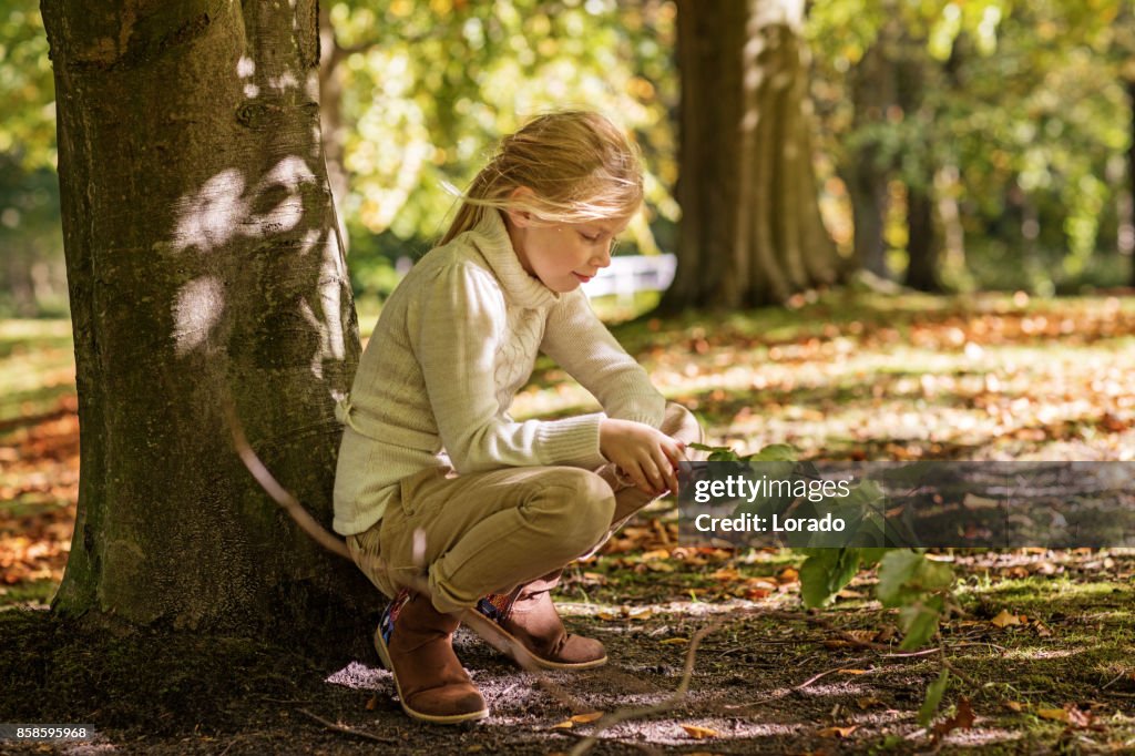 Beautiful young blond girl playing in trees in Autumnal Park