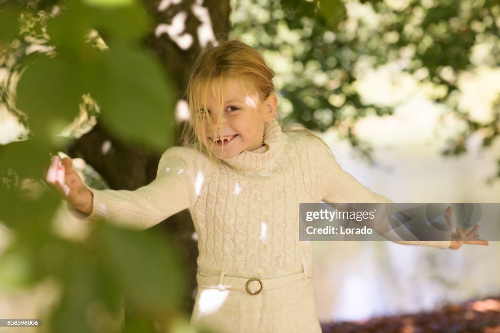 Linda garota loira jogando em árvores no parque outono