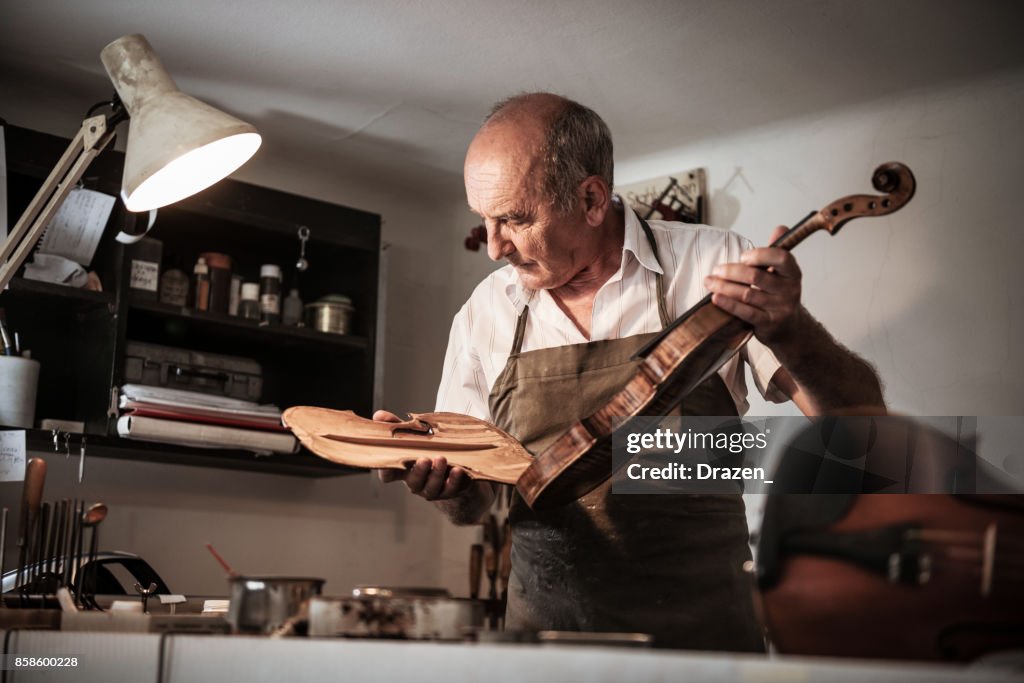 Senior Handwerker Violine Körper zu öffnen, um das Instrument zu überprüfen