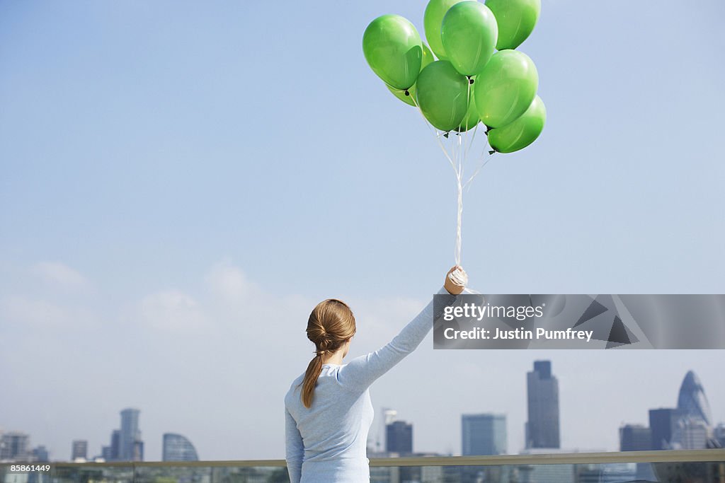 Woman holding balloons on rooftop, rear view