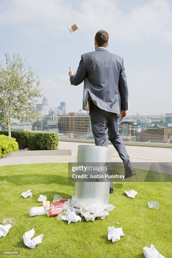 Businessman on rooftop by dustbin, rear view