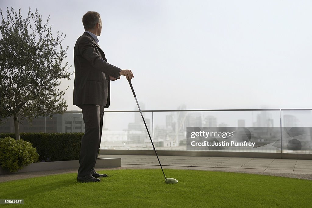 Businessman playing golf on rooftop, side view