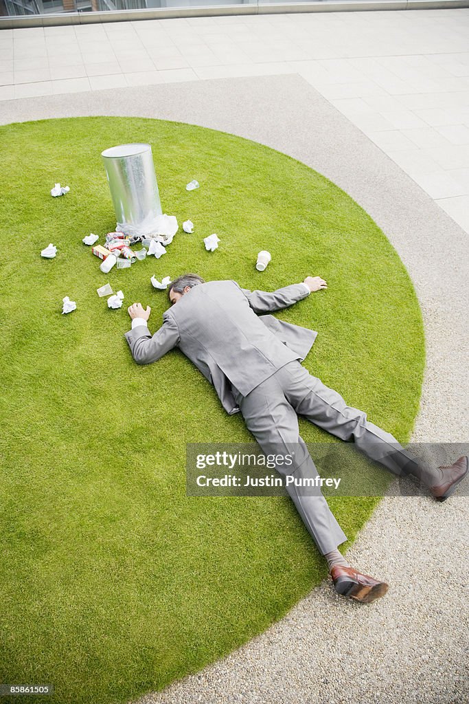 Businessman lying on grass by dustbin