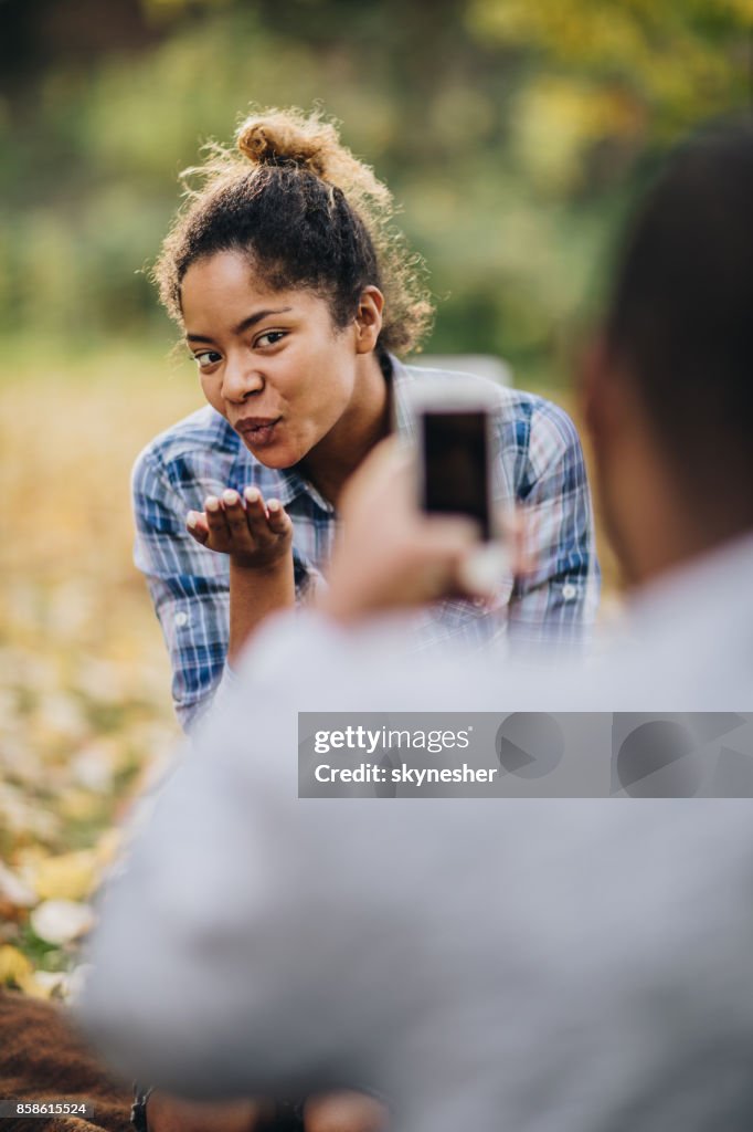 Zwarte vrouw blaast een kus terwijl wordt gefotografeerd in de natuur.