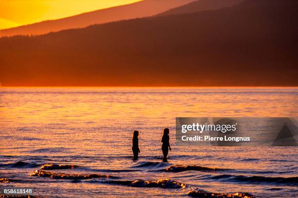nonrecognizable young girls playing in the sea at sunset, kitsina beach, vancouver, british columbia, canada - english bay stockfoto's en -beelden