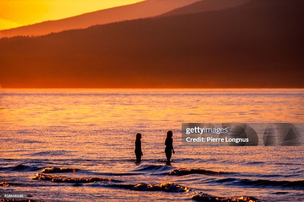 Nonrecognizable young girls playing in the sea at sunset, Kitsina Beach, Vancouver, British Columbia, Canada