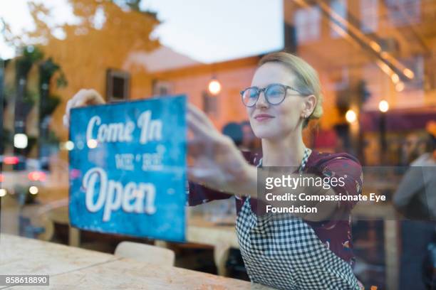 business owner setting up open sign in cafe window - begin stockfoto's en -beelden