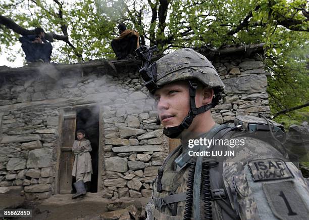 Soldier from 1st Infantry Division smokes as an Afghan boy looks at him during a mission of searching weapon cache in Nishagam, in Afghanistan's...