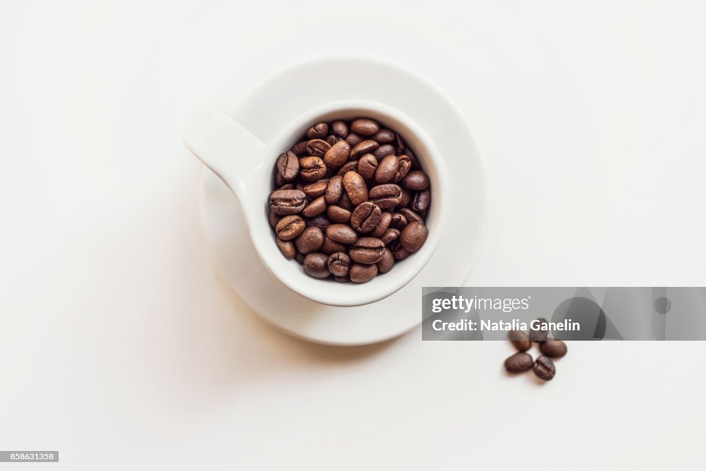 Cup of roasted coffee beans on white