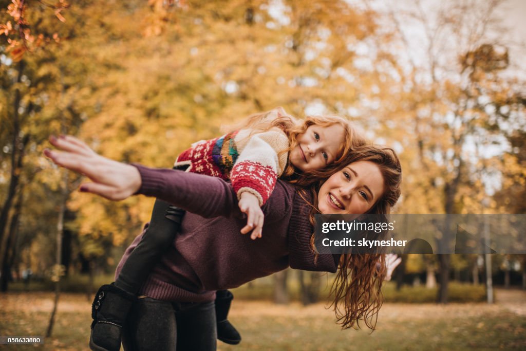 Playful redhead mother piggybacking her little daughter in nature.