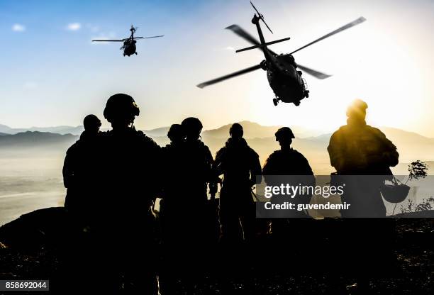 silhouettes of soldiers during military mission at dusk - milicia imagens e fotografias de stock